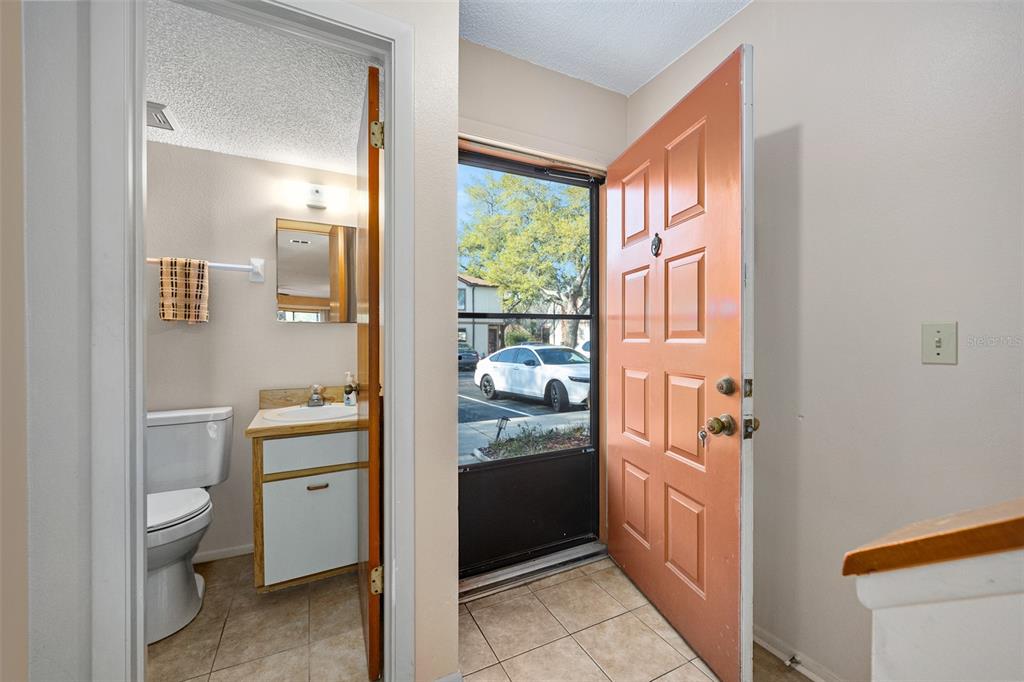 An open front door reveals a tiled entryway next to a small bathroom with a vanity — 149 WHITE FAWN DRIVE UNIT 1490, DAYTONA BEACH, FL