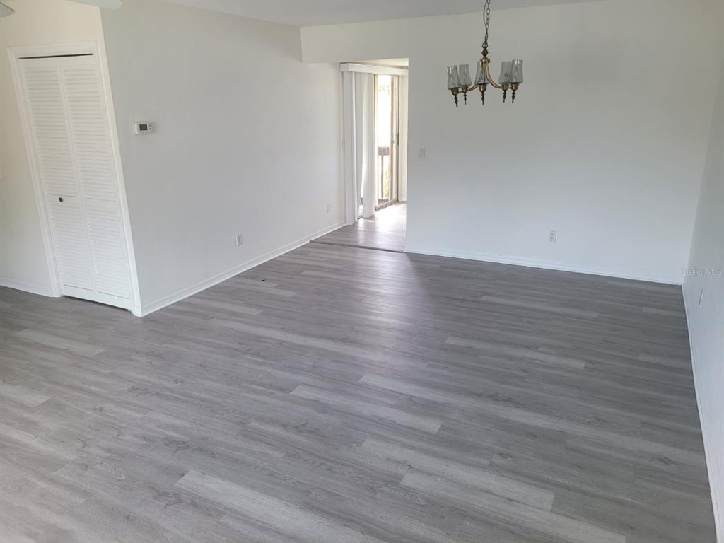 An empty room with gray wood-look flooring, white walls, a louvered closet, and a chandelier — 22481 WESTCHESTER BOULEVARD UNIT B35, PUNTA GORDA, FL