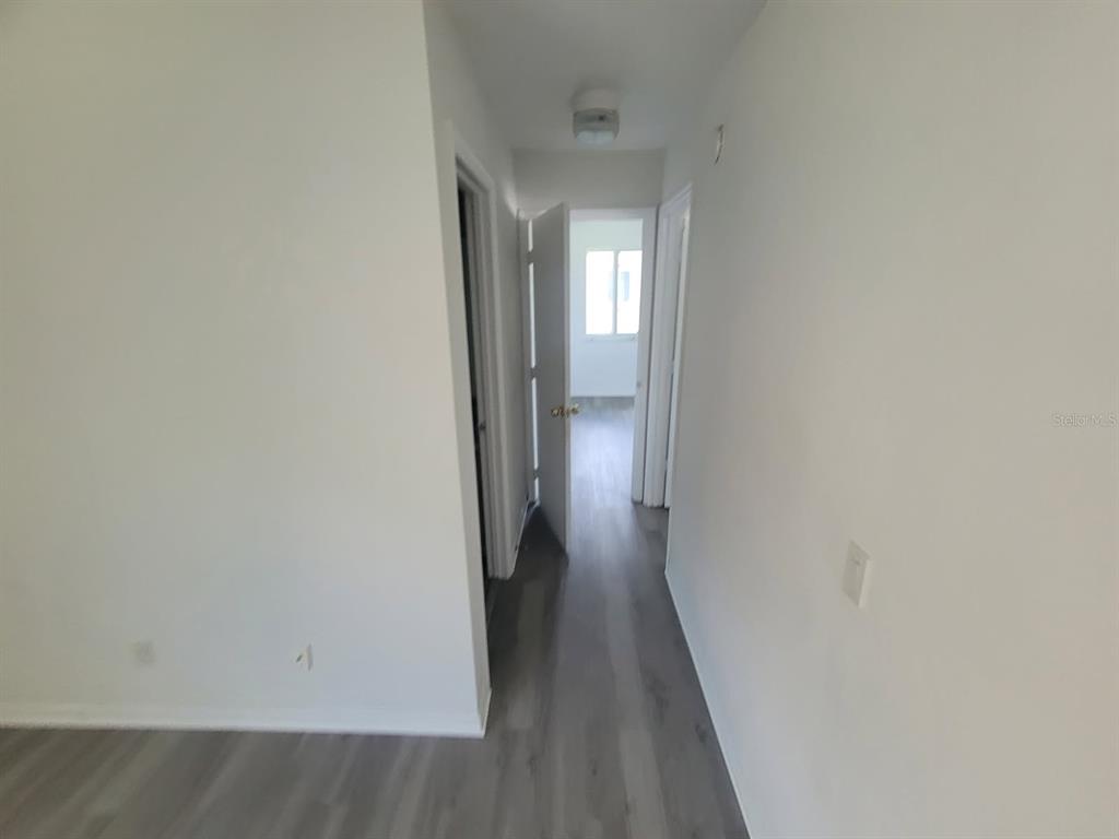 A hallway with light gray wood-look flooring leads to a room with a window — 22481 WESTCHESTER BOULEVARD UNIT B35, PUNTA GORDA, FL