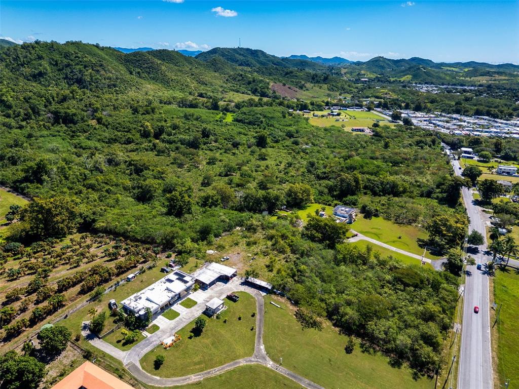 An aerial view shows a rural property with a house, outbuildings, and surrounding green hills — BO TIJERAS, JUANA DIAZ, PR