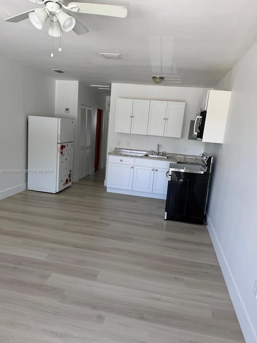 A kitchen features white cabinets, a black stove, a white refrigerator, and light wood flooring — 4840 NW 27th Ave # 2, Miami FL 33142, MIAMI, FL