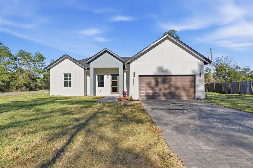 A modern single-story house with white board-and-batten siding, a gray entryway, and a paved driveway — 3699 SW 169TH PLACE, OCALA, FL