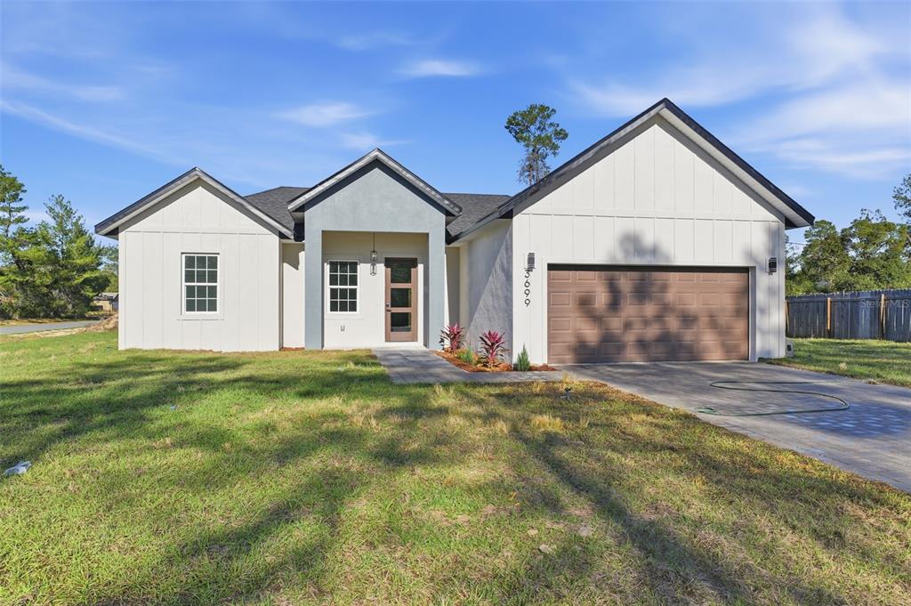 A single-story house with white board-and-batten siding, a gray stucco entryway, and a two-car garage — 3699 SW 169TH PLACE, OCALA, FL
