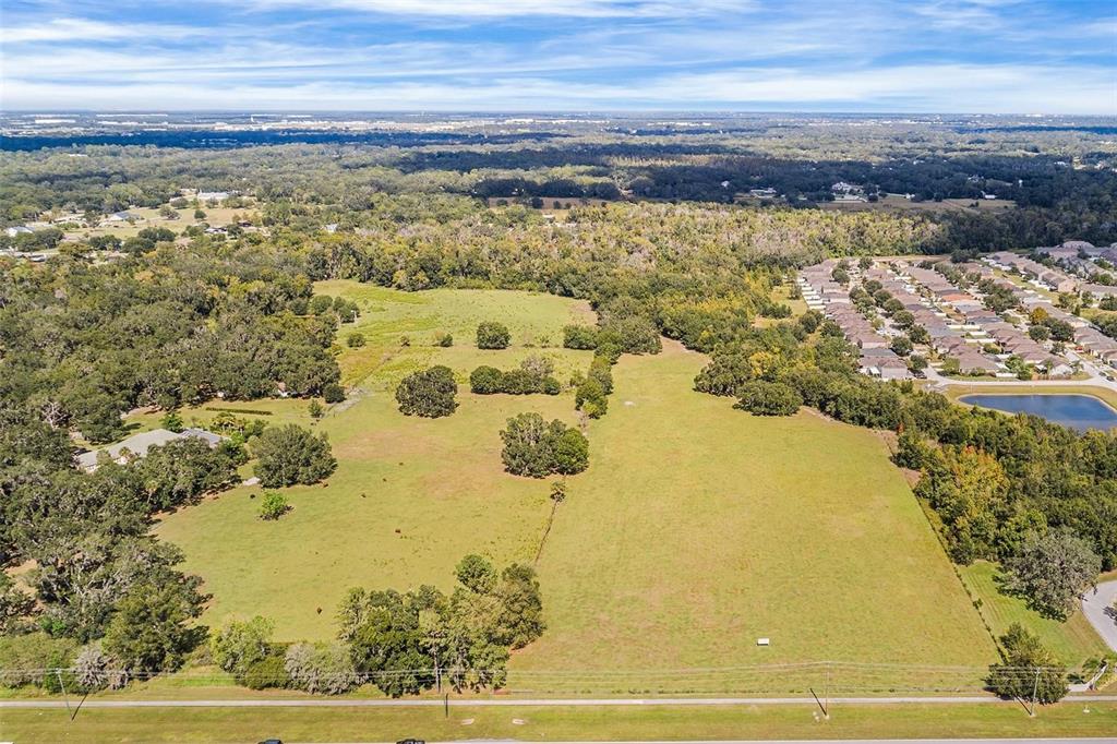 An aerial view shows a large, grassy, undeveloped lot bordered by trees and a residential neighborhood — 2523 SHEPHERD ROAD, LAKELAND, FL