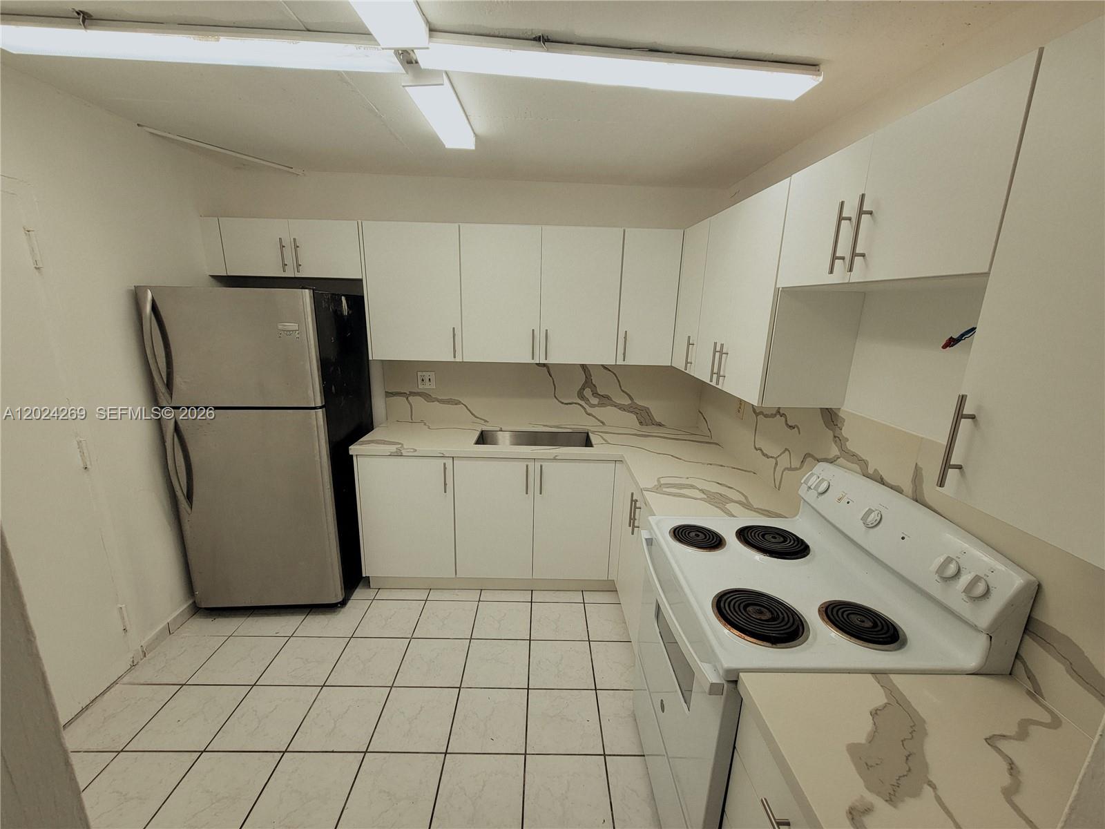 A kitchen features white cabinets, marble-patterned countertops, a stainless steel refrigerator, and white tile flooring — 13701 Kendale Lakes Cir # 112, Miami FL 33183, MIAMI, FL