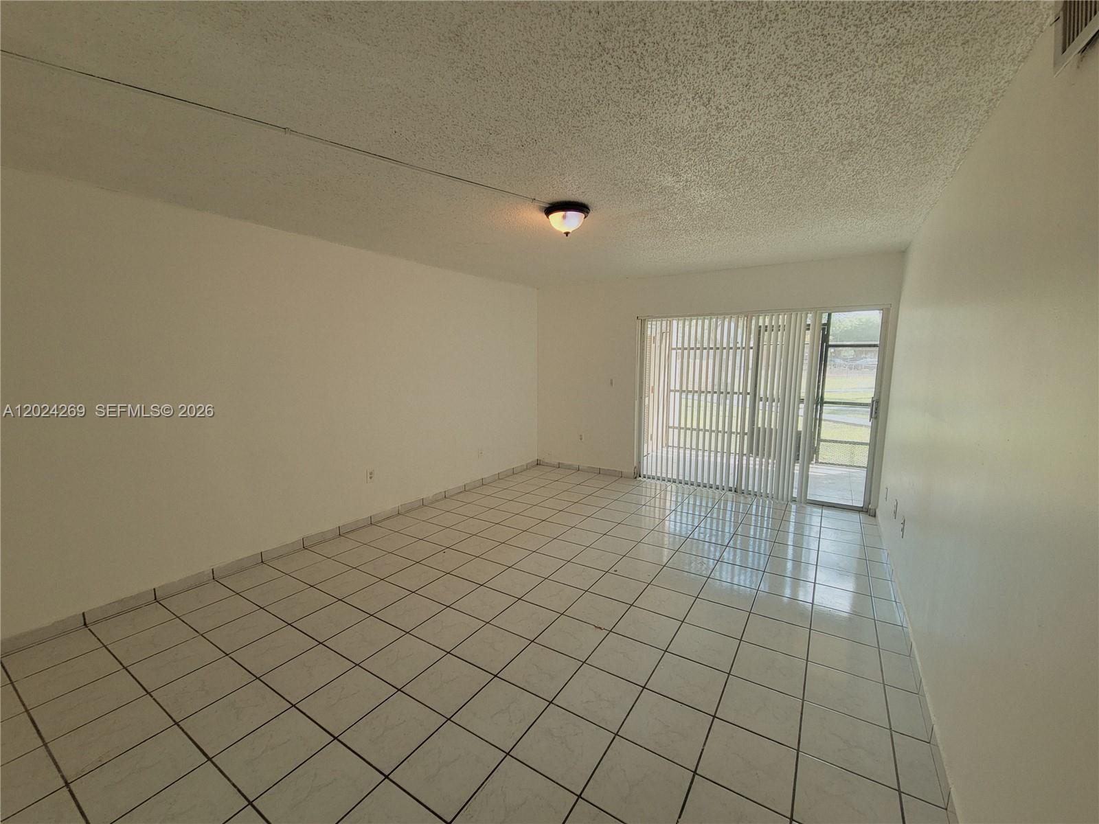 An empty room features white tiled floors, a popcorn ceiling, and sliding glass patio doors — 13701 Kendale Lakes Cir # 112, Miami FL 33183, MIAMI, FL