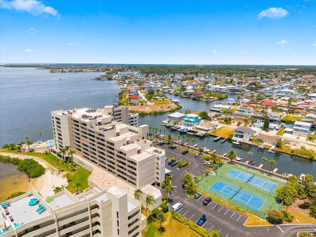 An aerial view shows a multi-story apartment building, tennis courts, and a coastal residential neighborhood — 6035 SEA RANCH DRIVE UNIT 100, HUDSON, FL