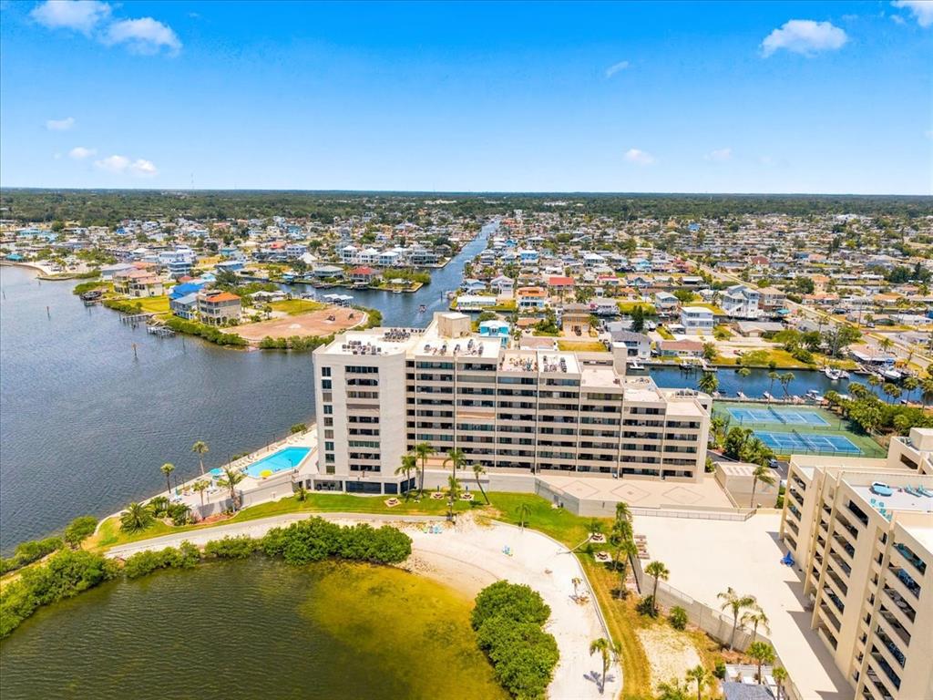 An aerial view shows a multi-story apartment building situated on a waterfront peninsula — 6035 SEA RANCH DRIVE UNIT 100, HUDSON, FL