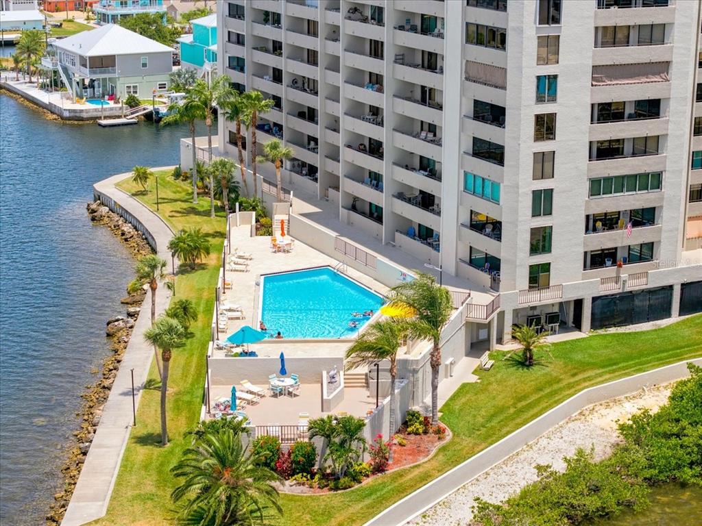 An aerial view shows a swimming pool and patio area adjacent to a tall apartment building — 6035 SEA RANCH DRIVE UNIT 100, HUDSON, FL