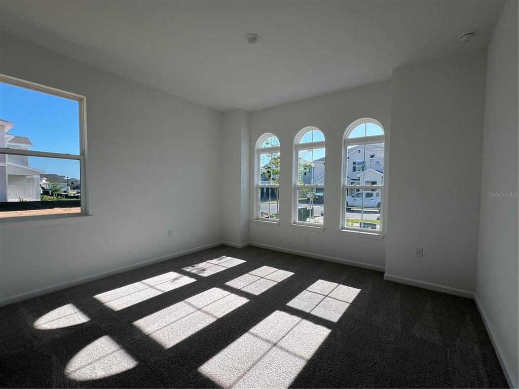 An empty bedroom with gray carpet, white walls, and several windows with arched tops — 2391 JUNIPER BERRY DRIVE, MINNEOLA, FL