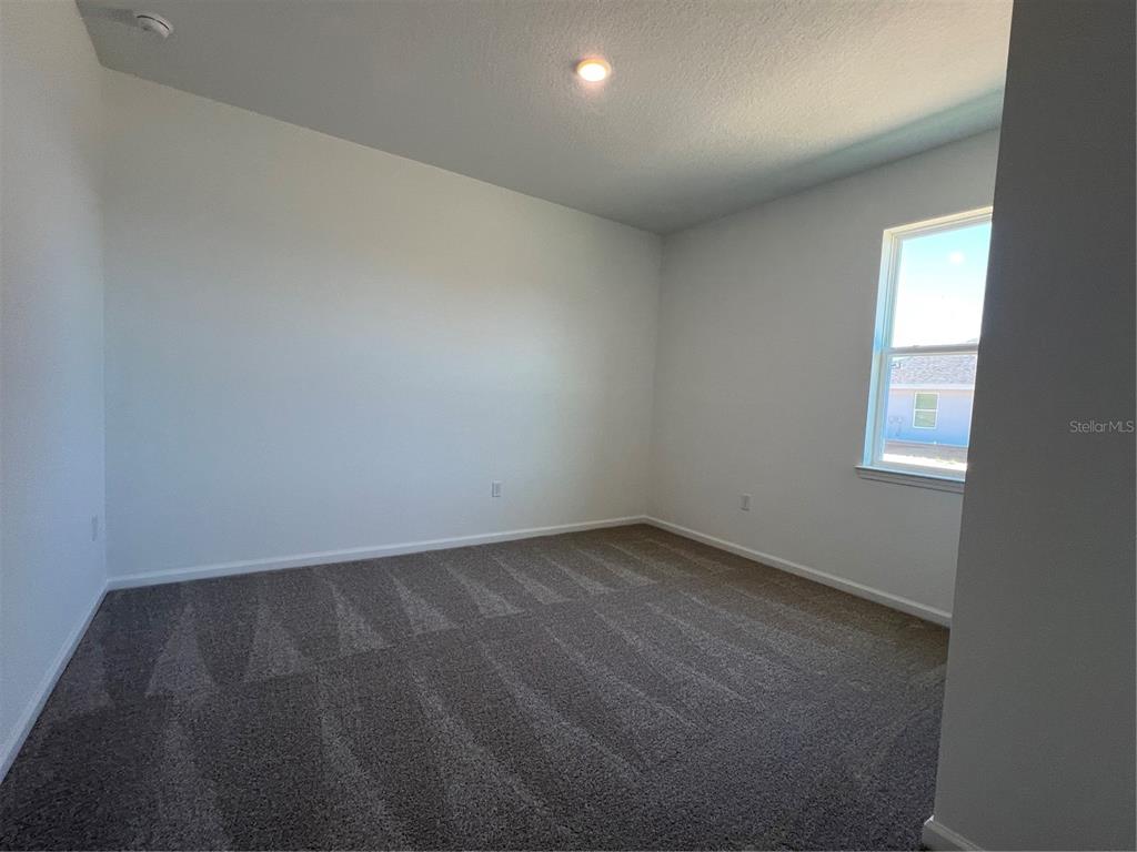 An empty bedroom features white walls, gray carpet, and a single window — 2391 JUNIPER BERRY DRIVE, MINNEOLA, FL