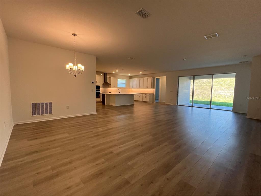 An open-concept living area features light wood flooring, a kitchen with an island, and sliding doors — 2391 JUNIPER BERRY DRIVE, MINNEOLA, FL