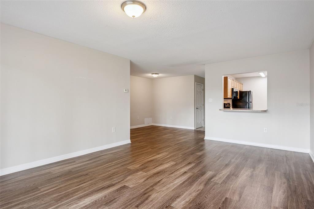 An empty living room with wood-look flooring, beige walls, and a kitchen pass-through window — 1695 LEE ROAD UNIT A116, WINTER PARK, FL