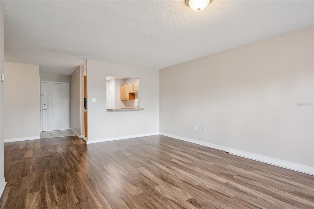 An empty living room features wood-look flooring, light-colored walls, and a kitchen pass-through window — 1695 LEE ROAD UNIT A116, WINTER PARK, FL