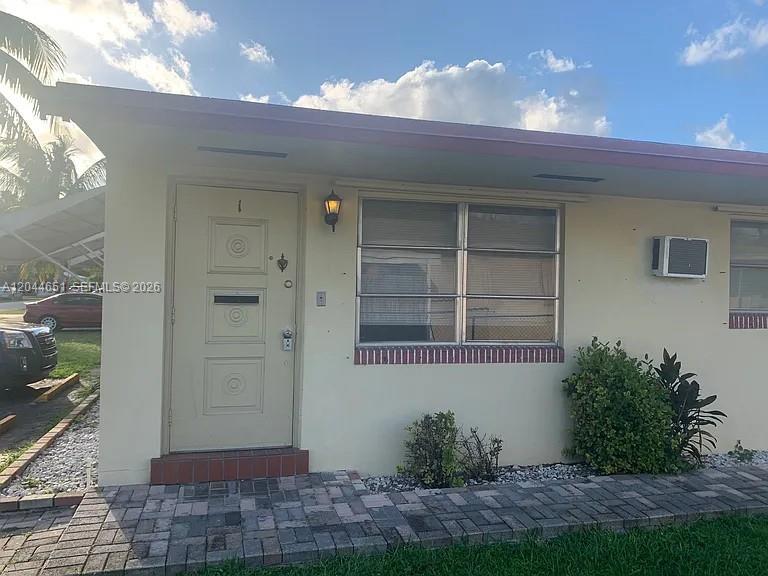 The exterior of a single-story building features a beige door, a window, and a walkway — 2407 Mckinley St # 2, Hollywood FL 33020, HOLLYWOOD, FL