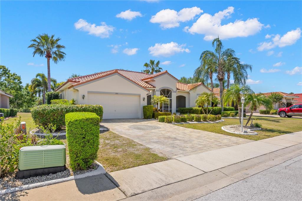 A single-story house with a tiled roof, paved driveway, and palm trees under a blue sky — 1305 CRYSTAL GREENS DRIVE, SUN CITY CENTER, FL