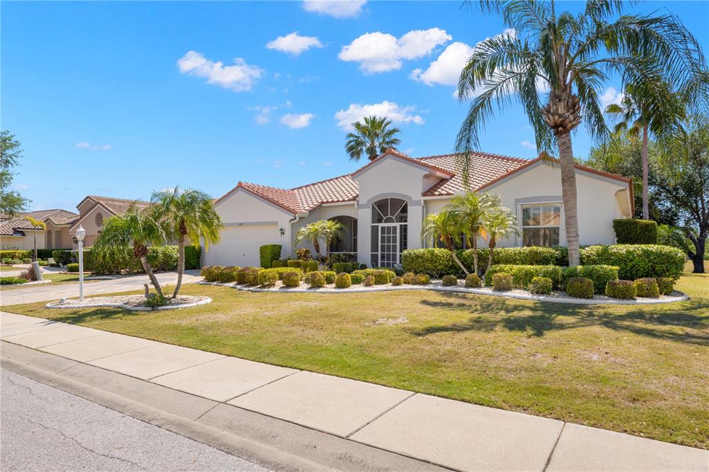 A single-story stucco house with a tile roof, palm trees, and a landscaped front yard — 1305 CRYSTAL GREENS DRIVE, SUN CITY CENTER, FL