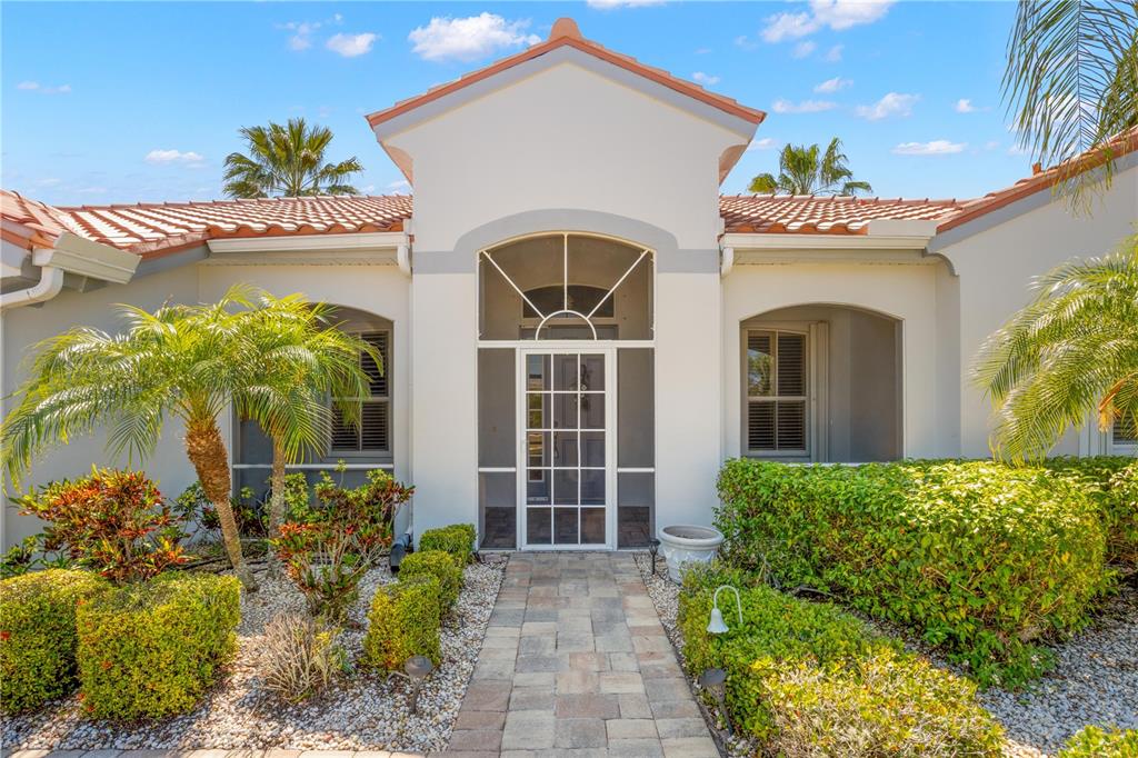 A paved walkway leads to the screened front entrance of a single-story stucco home — 1305 CRYSTAL GREENS DRIVE, SUN CITY CENTER, FL