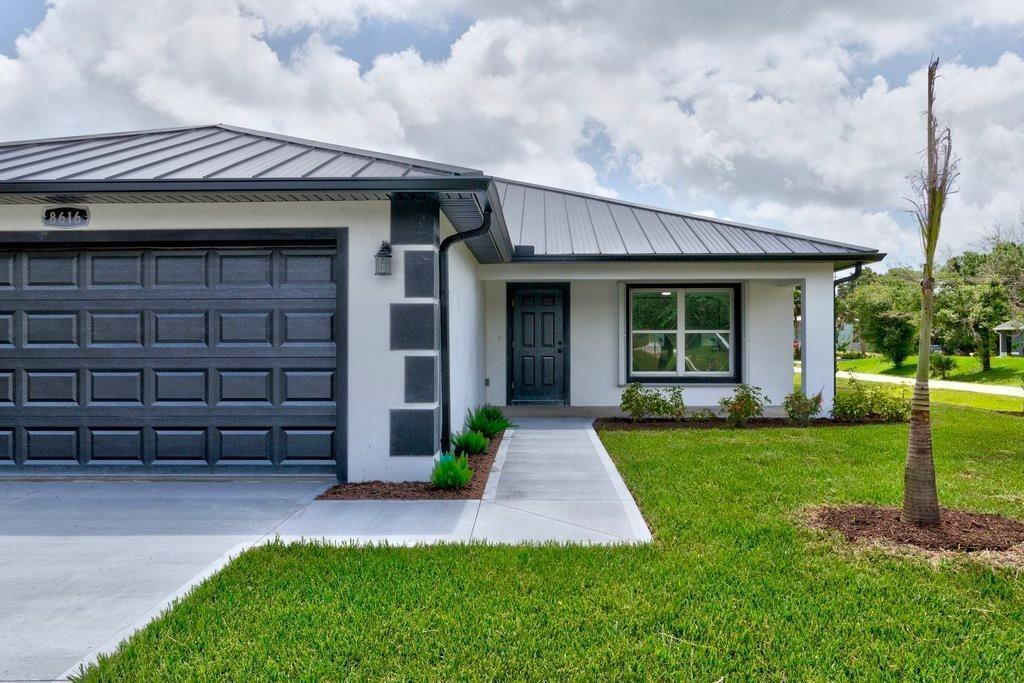 A single-story house exterior features a dark metal roof, white stucco walls, and a garage — VERO BEACH, FL
