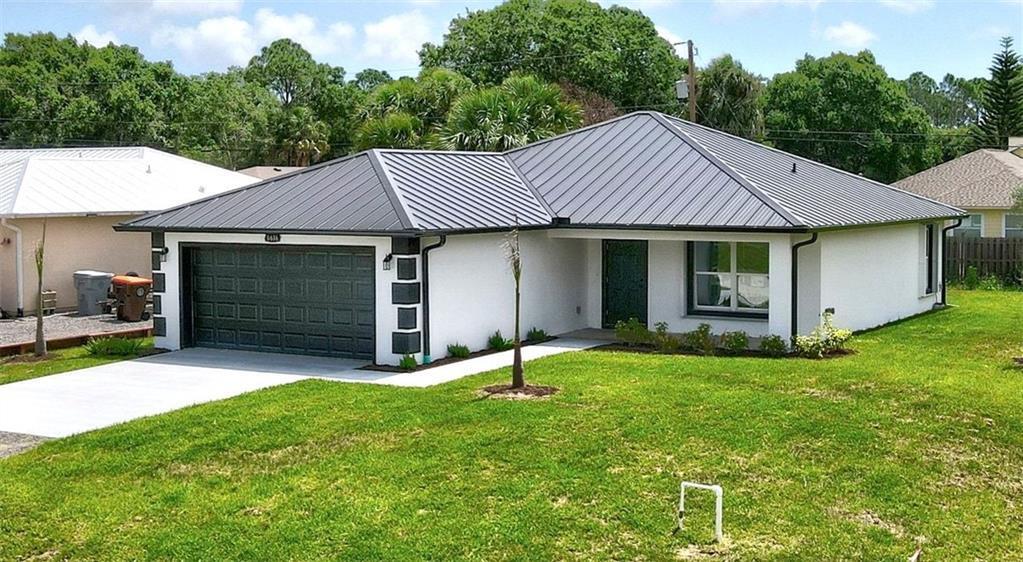 A single-story house with a white stucco exterior, dark metal roof, and a two-car garage — VERO BEACH, FL