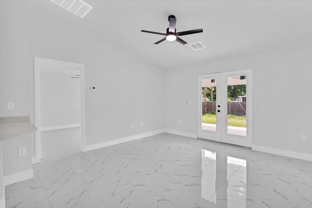 An empty room with white marble-patterned tile floors, a ceiling fan, and glass French doors — VERO BEACH, FL