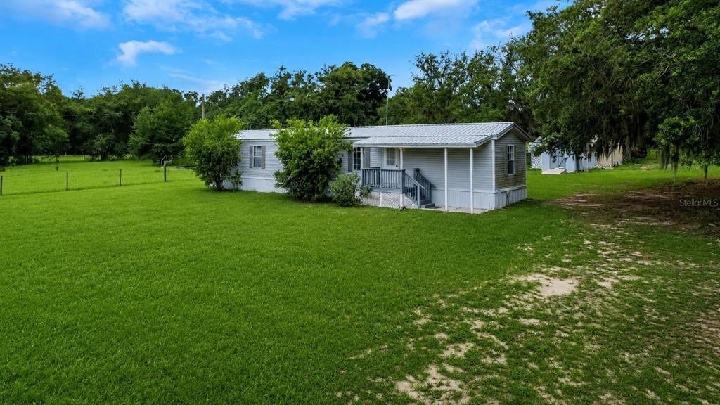 A light-colored mobile home sits on a large grassy lot surrounded by trees — 7438 CR 663, BUSHNELL, FL