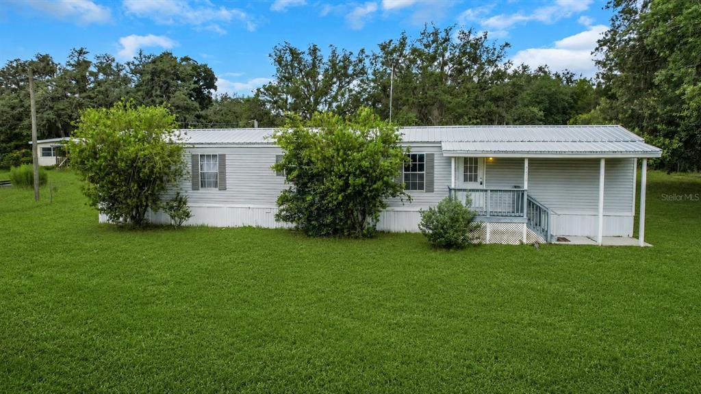 A single-story manufactured home with light gray siding sits on a large, grassy lot — 7438 CR 663, BUSHNELL, FL