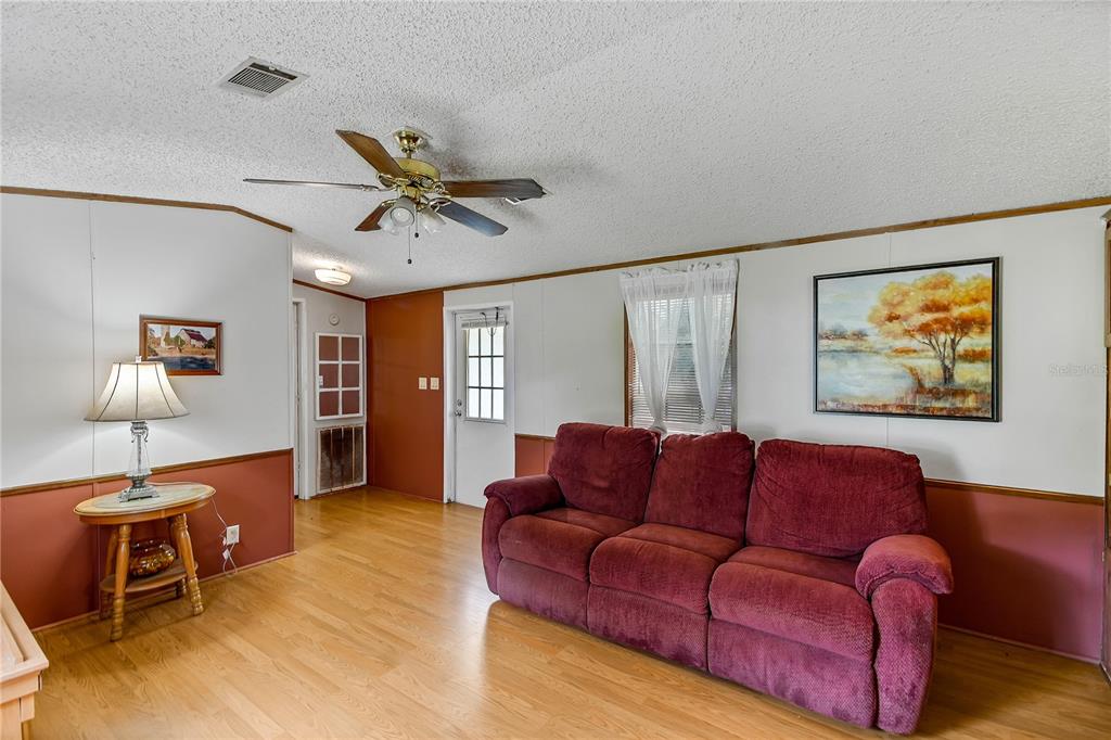 A living room features wood-look flooring, a red sofa, a ceiling fan, and white walls — 7438 CR 663, BUSHNELL, FL