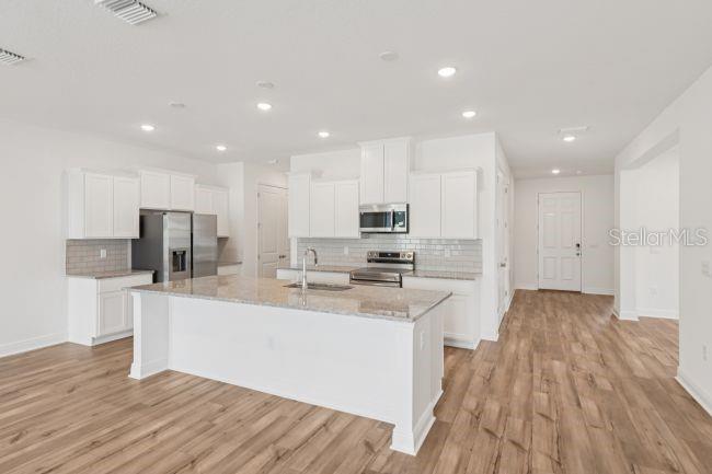 A modern kitchen features white cabinets, a large granite-topped island, and light wood-look flooring — 10 ASTERS COURT, HOMOSASSA, FL