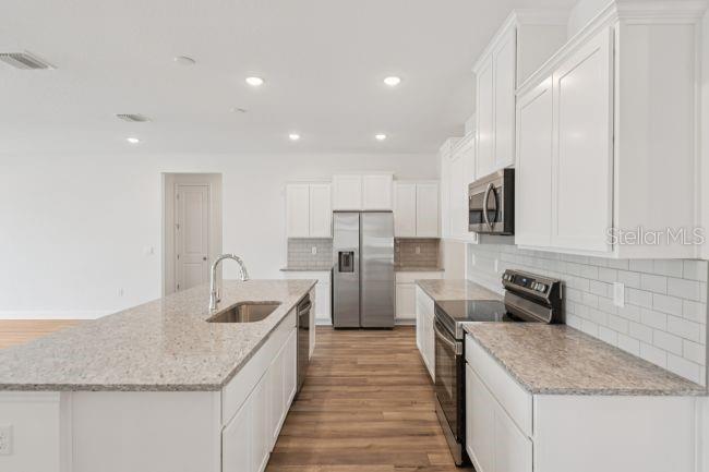 A modern kitchen features white cabinets, granite countertops, stainless steel appliances, and wood-look flooring — 10 ASTERS COURT, HOMOSASSA, FL