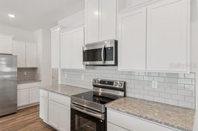 A kitchen features white cabinets, granite countertops, stainless steel appliances, and a gray subway tile backsplash — 10 ASTERS COURT, HOMOSASSA, FL