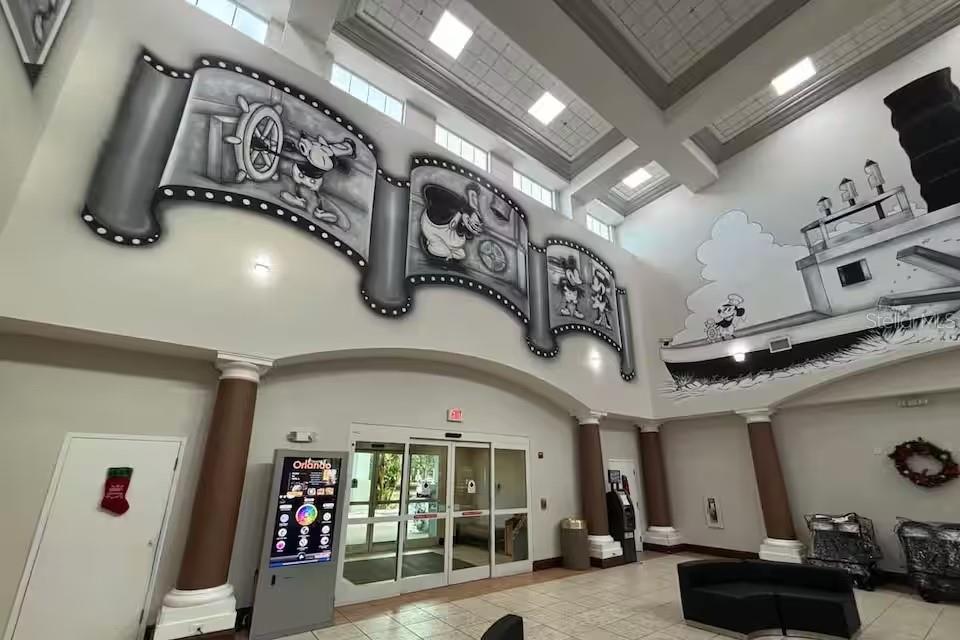A lobby features high ceilings, a large Mickey Mouse mural, and glass sliding entrance doors — 8303 PALM PARKWAY UNIT 208, ORLANDO, FL