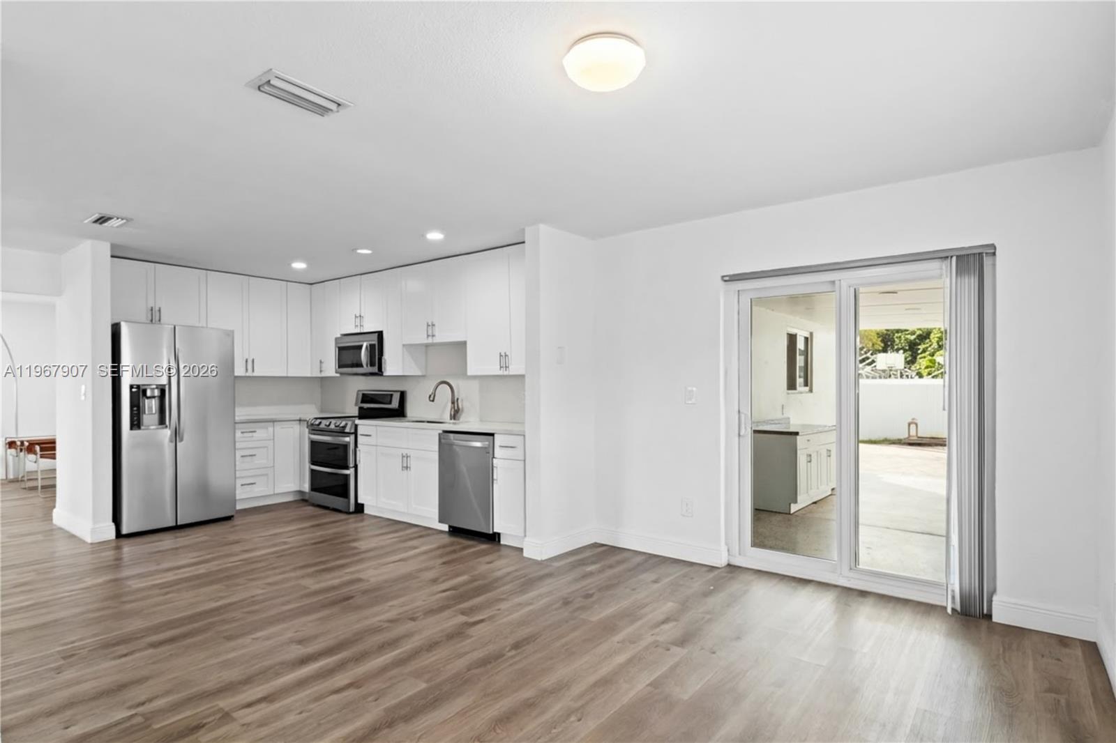 A kitchen with white cabinets and stainless steel appliances opens to a patio through sliders — 10360 SW 24th St, Miami FL 33165, MIAMI, FL