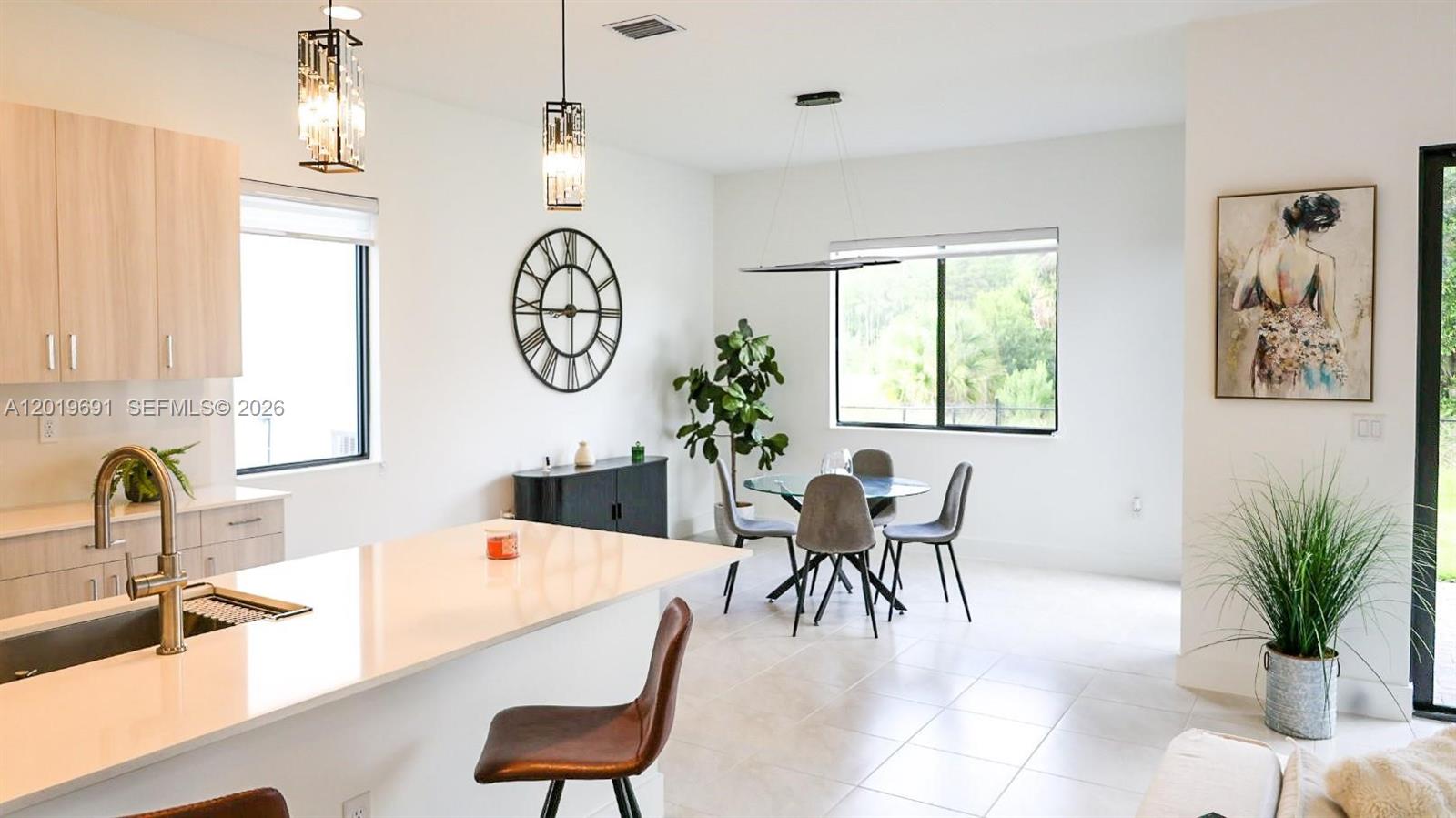 A modern kitchen with a white island and dining area featuring a glass table — 5868 Agostino Way, Ave Maria FL 34142, AVE MARIA, FL