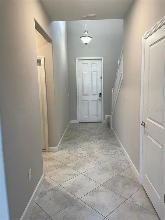 An entryway with light gray walls, tile flooring, a white front door, and a staircase — 9671 IVORY DRIVE, SUN CITY CENTER, FL