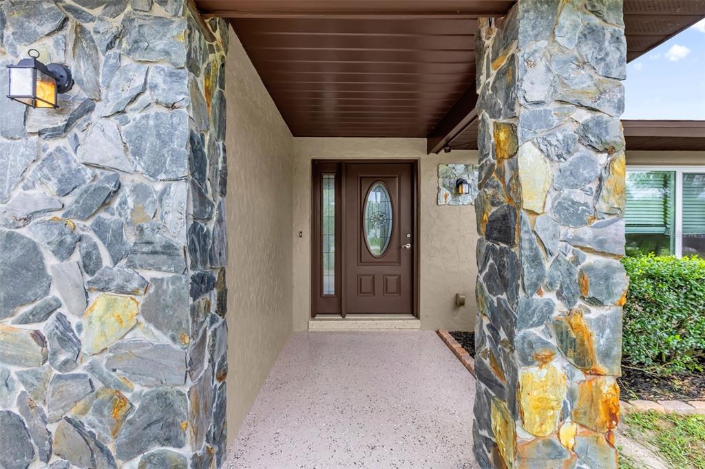 A covered entryway features stone-clad pillars, a brown front door with a glass insert, and speckled flooring — 5202 SYDNEY ROAD, FRUITLAND PARK, FL