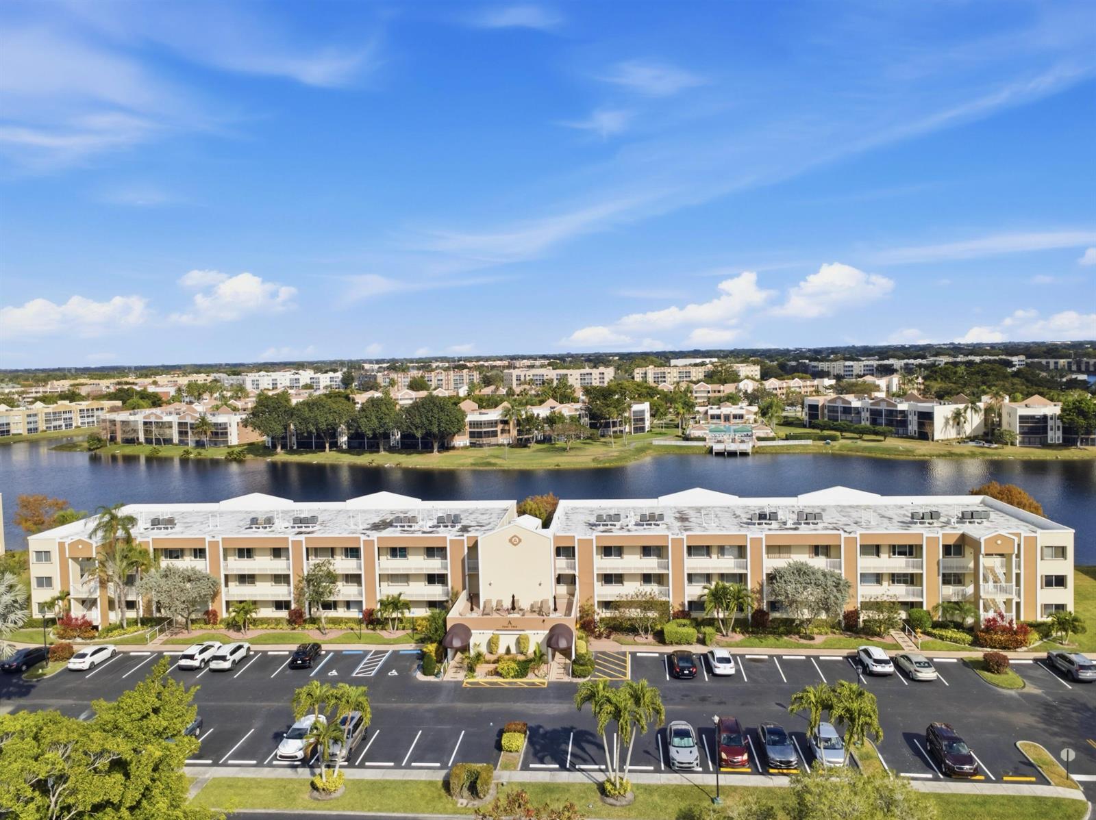 An aerial view shows a multi-story apartment building with a parking lot and a lake — 7292 S Devon Drive # 302, Tamarac FL 33321, TAMARAC, FL