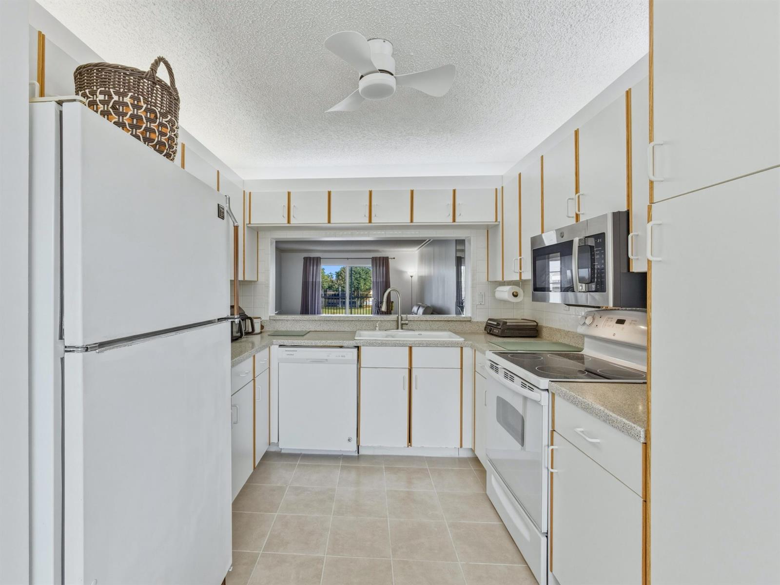 A white kitchen features a pass-through window, tile flooring, and a ceiling fan — 7292 S Devon Drive # 302, Tamarac FL 33321, TAMARAC, FL