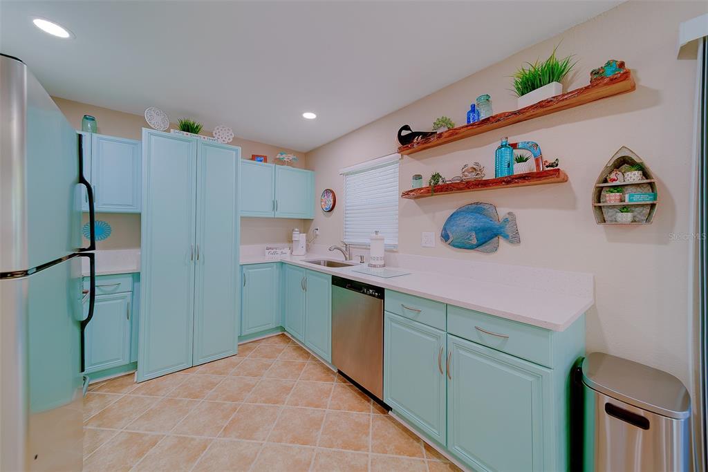 A kitchen features light blue cabinets, white countertops, stainless steel appliances, and rustic wood shelving — 13125 WILCOX ROAD UNIT 16105, LARGO, FL