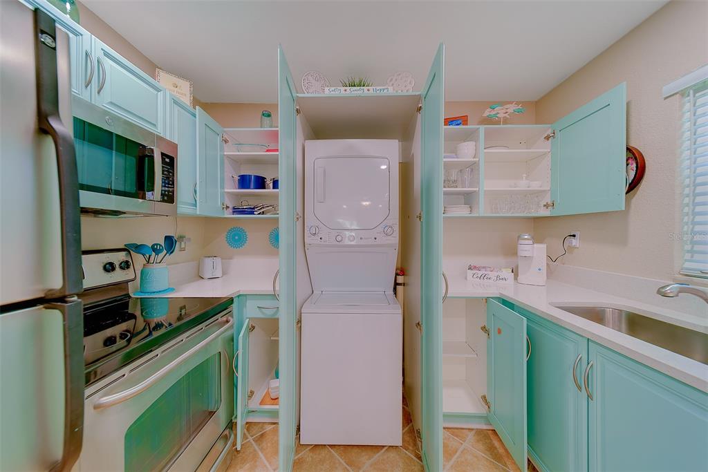 A kitchen features teal cabinets, stainless steel appliances, and a stacked washer-dryer unit — 13125 WILCOX ROAD UNIT 16105, LARGO, FL