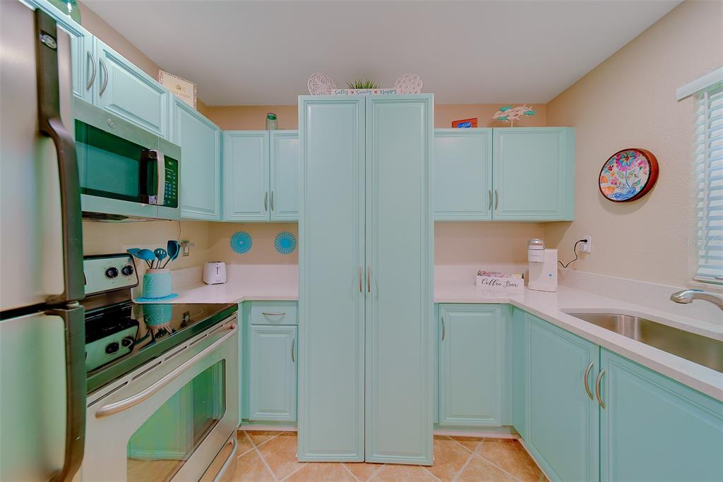A kitchen features light blue cabinets, white countertops, stainless steel appliances, and tile flooring — 13125 WILCOX ROAD UNIT 16105, LARGO, FL