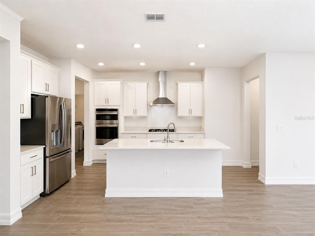 A modern kitchen features white cabinetry, stainless steel appliances, a center island, and wood-look flooring — 11757 71ST AVENUE E, PALMETTO, FL