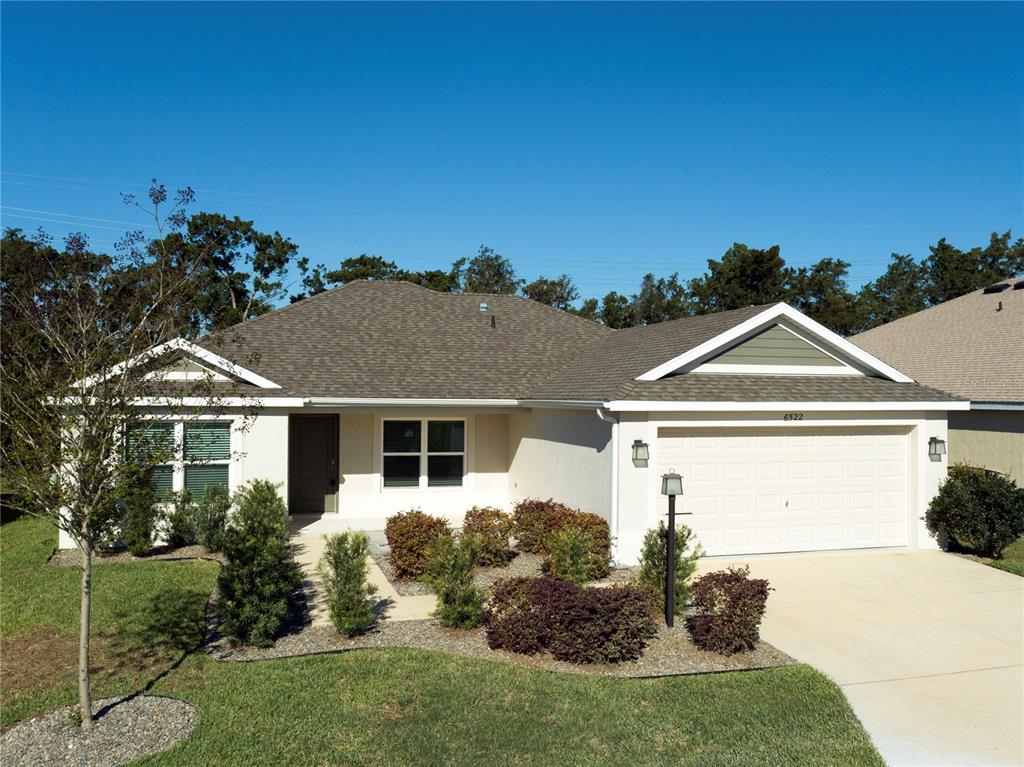 A single-story house with a beige stucco exterior, a shingled roof, and a two-car garage — 6522 MCKNIGHT LOOP, THE VILLAGES, FL