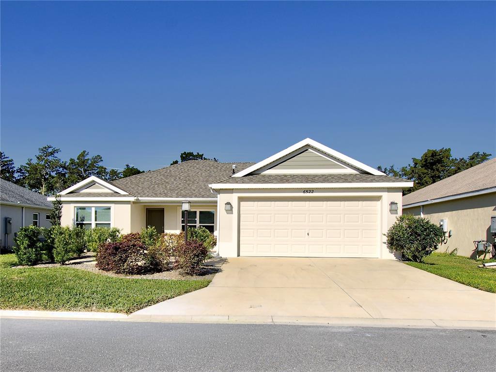 A single-story house with a two-car garage, beige stucco siding, and a tan shingled roof — 6522 MCKNIGHT LOOP, THE VILLAGES, FL