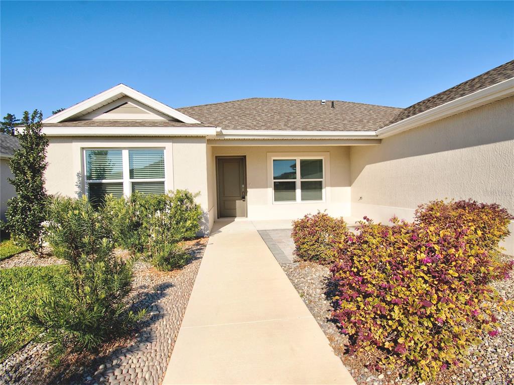 A beige single-story house features a concrete walkway leading to a front door — 6522 MCKNIGHT LOOP, THE VILLAGES, FL