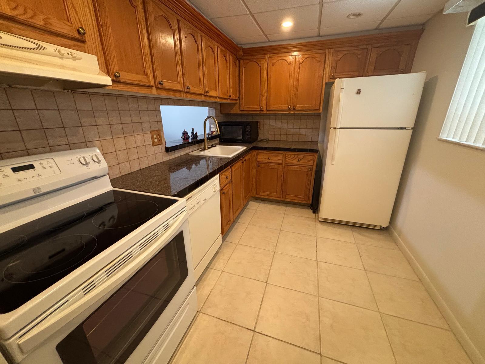 A kitchen features oak cabinets, dark granite countertops, white appliances, and light-colored tile flooring — 5340 Las Verdes Circle # 222, Delray Beach FL 33484, DELRAY BEACH, FL