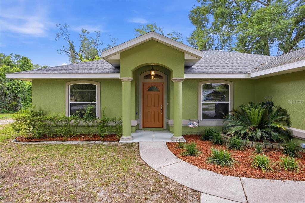A green single-story house features a covered entryway with two columns and an orange door — 3539 SE 136TH PLACE, SUMMERFIELD, FL