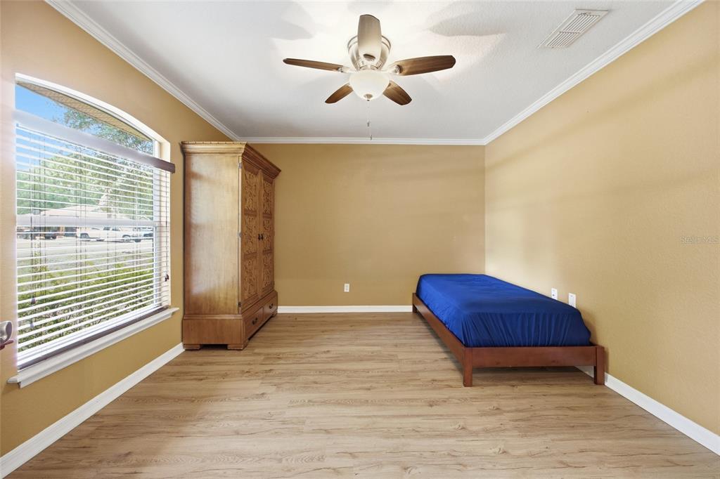A bedroom with tan walls, wood-look flooring, a ceiling fan, an armoire, and a bed — 3539 SE 136TH PLACE, SUMMERFIELD, FL