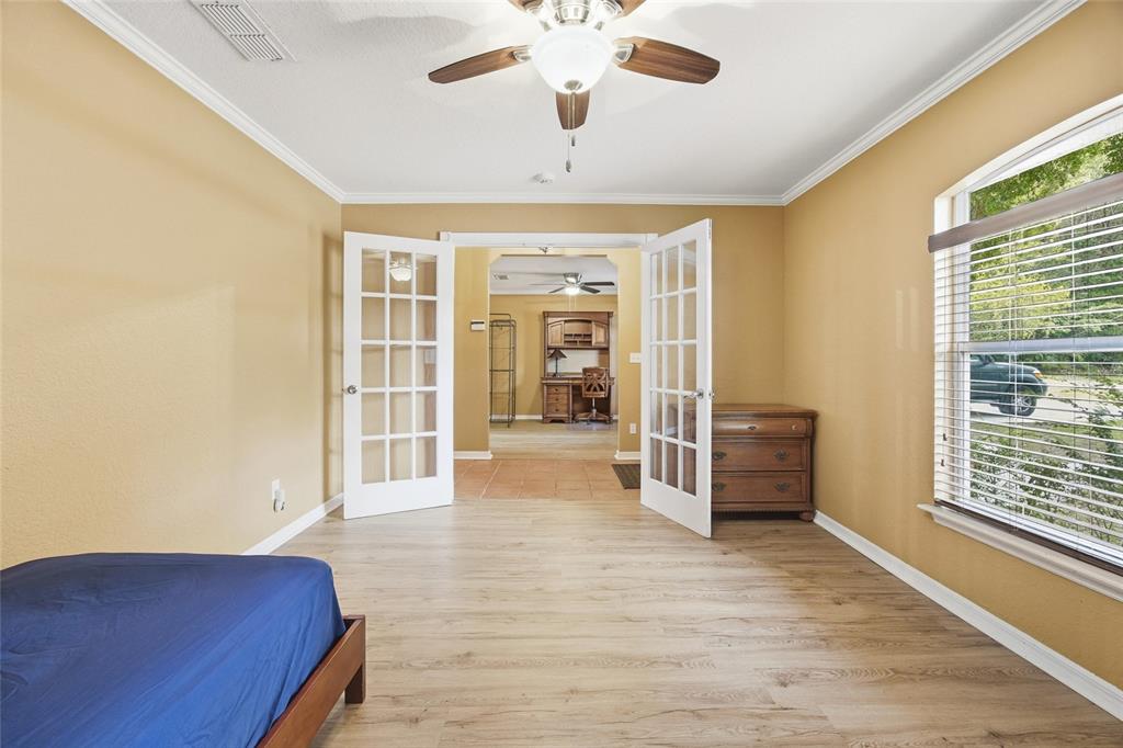 A bedroom with light wood-look flooring, yellow walls, and French doors leading to an office — 3539 SE 136TH PLACE, SUMMERFIELD, FL