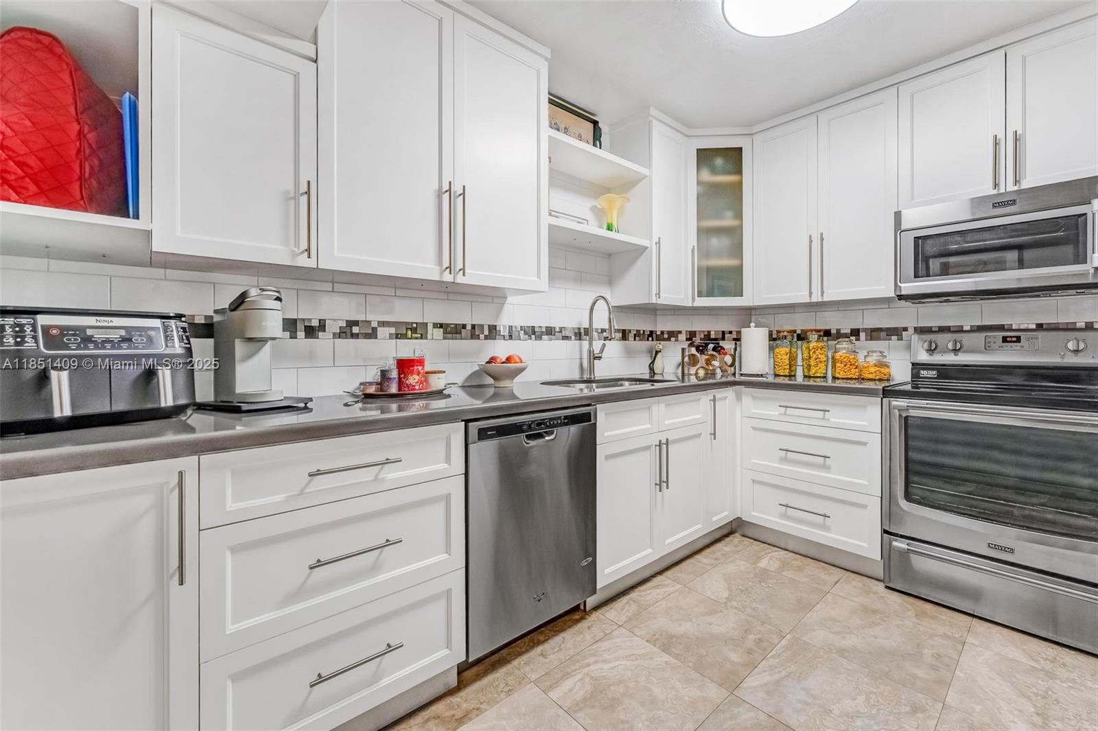 A kitchen features white cabinets, stainless steel appliances, a tiled backsplash, and light-colored floor tiles — 4330 Hillcrest Dr # 516, Hollywood FL 33021, HOLLYWOOD, FL